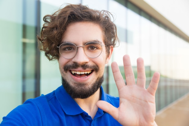 Gelukkig vrolijke man draagt een bril, hallo zwaaien