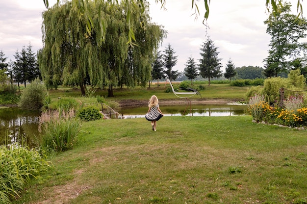 Gratis foto gelukkig vrouwelijk kind staat voor een vijver in de prachtige tuin