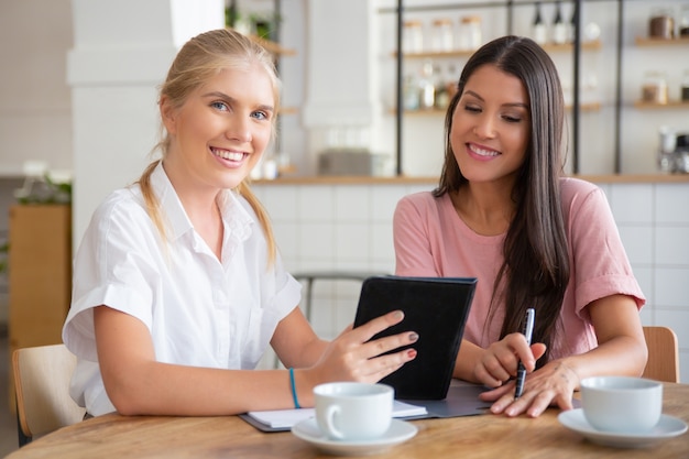 Gelukkig vrouwelijke agent en klantbijeenkomst tijdens kopje koffie, samen met behulp van tablet,