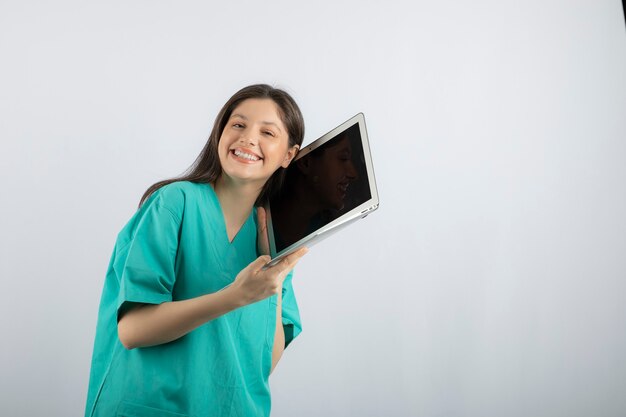 Gelukkig vrouwelijke verpleegster poseren met laptop op wit.