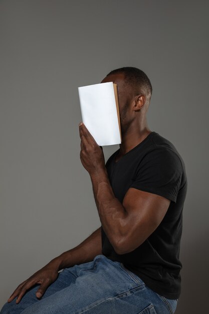 Gelukkig wereldboek en auteursrechtdag, lees om iemand anders te worden - man bedekt gezicht met boek tijdens het lezen op grijze muur.