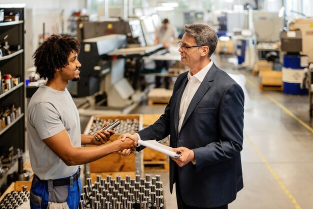 Gelukkig zakenman begroet Afro-Amerikaanse staalarbeider tijdens een bezoek aan industriële faciliteit