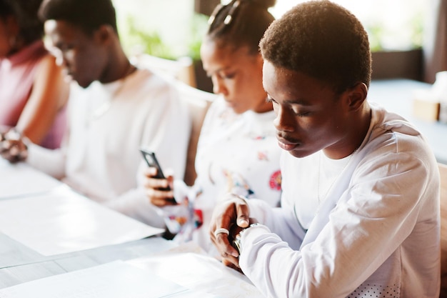 Gelukkige afrikaanse vrienden zitten en kletsen in café Groep zwarte mensen ontmoeten elkaar in restaurant en kijken naar hun mobiele telefoon