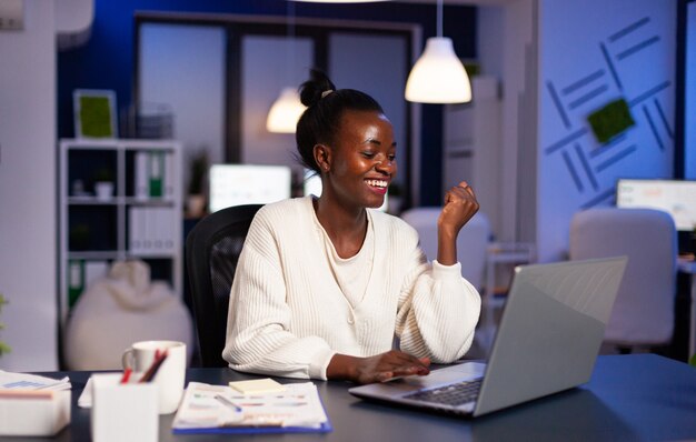 Gelukkige Afrikaanse vrouw na het lezen van e-mail met goed nieuws die 's avonds laat werkt