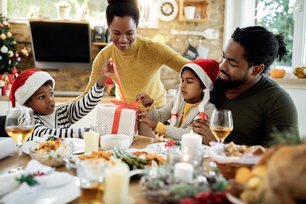 Gelukkige Afro-Amerikaanse familie die kerstcadeautjes opent aan de eettafel