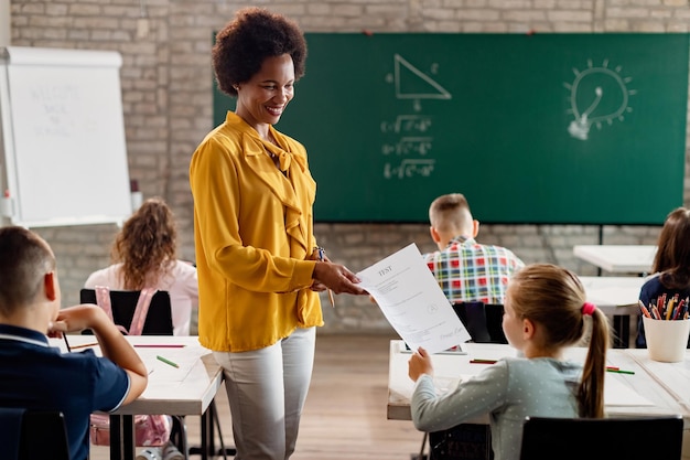 Gelukkige Afro-Amerikaanse leraar die testresultaten geeft aan elementaire student in de klas