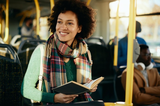 Gratis foto gelukkige afro-amerikaanse vrouw die een boek leest terwijl ze met de bus reist