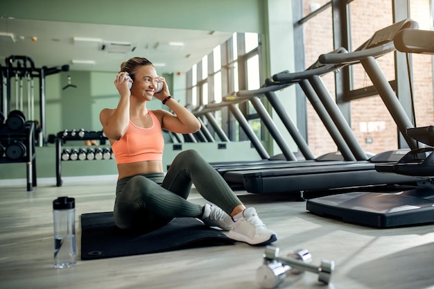 Gelukkige atletische vrouw die muziek luistert op een koptelefoon in een sportschool