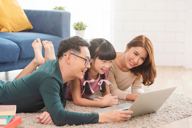 Gelukkige Aziatische familie die computerlaptop samen op bank thuis met behulp van woonkamer.