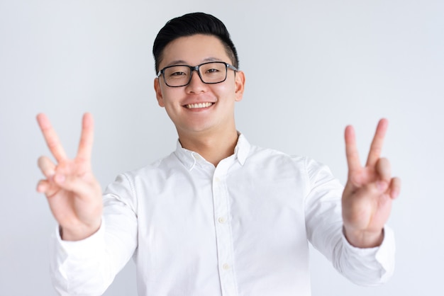Gelukkige Aziatische mens die twee overwinningstekens toont
