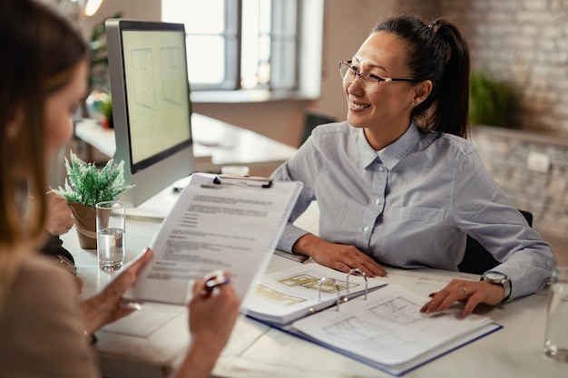 Gelukkige Aziatische verzekeringsagent die met haar klanten communiceert tijdens een vergadering op kantoor