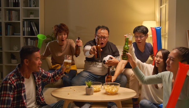 Gelukkige aziatische vrienden of voetbalfans die voetbal op tv kijken en de overwinning thuis vieren Vriendschapssport- en entertainmentconcept