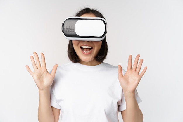 Gelukkige aziatische vrouw die een VR-headset gebruikt, met opgeheven handen zwaait en lacht met een virtual reality-bril die op een witte achtergrond staat