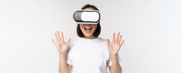 Gelukkige aziatische vrouw die een VR-headset gebruikt, met opgeheven handen zwaait en lacht met een virtual reality-bril die op een witte achtergrond staat