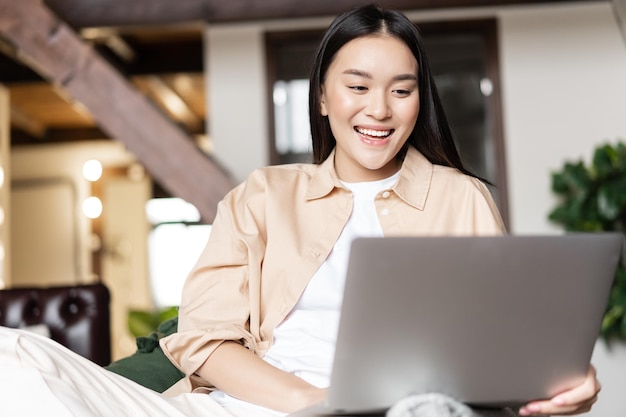 Gelukkige aziatische vrouw die thuis rust met een laptop die video's bekijkt of een website op de computer bekijkt