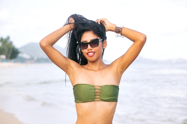 Gelukkige Aziatische vrouw met magere figuur plezier op tropisch strand. het dragen van stijlvolle bikini en zonnebril.