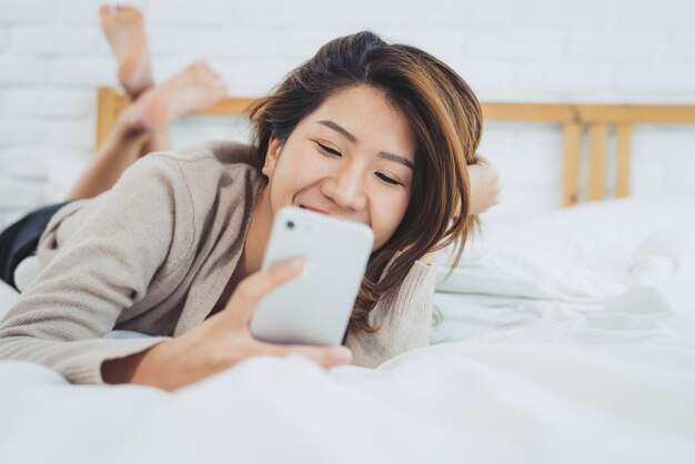 Gelukkige Aziatische vrouwen gebruiken slimme telefoon op het bed in ochtend