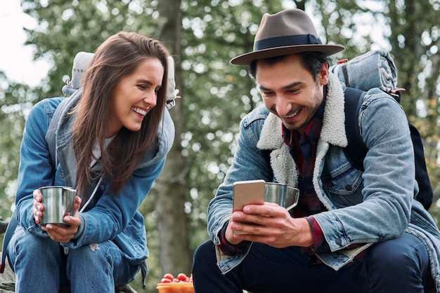 Gelukkige backpackers die koffie drinken en mobiele telefoon gebruiken