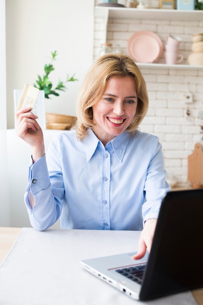 Gelukkige bedrijfsvrouw die laptop en creditcard met behulp van