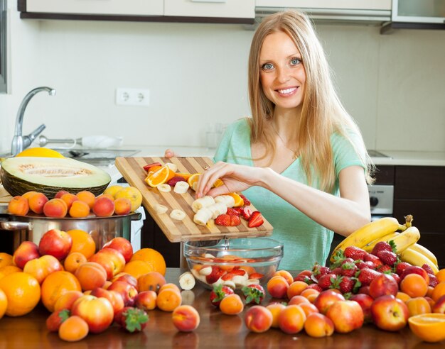 Gelukkige blonde vrouw koken met rijpe vruchten