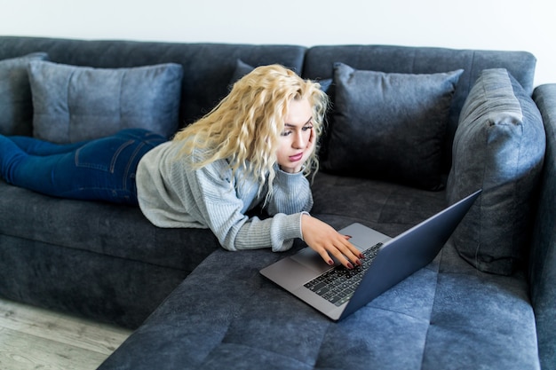 Gelukkige blondevrouw die aan een laptop zitting op de laag in het huis werkt.