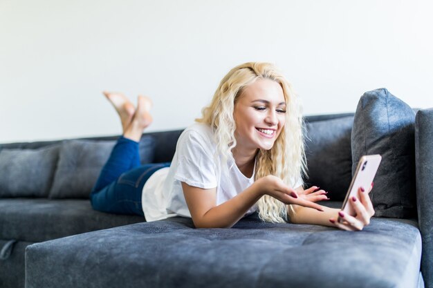 Gelukkige blondezitting op haar bank op de telefoon thuis