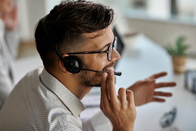 Gelukkige callcenteragent die een headset draagt terwijl hij met klanten praat en op kantoor werkt