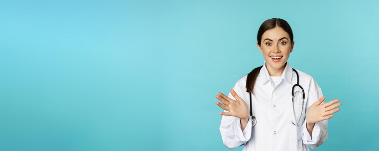 Gratis Foto gelukkige en opgewonden glimlachende jonge vrouw op zoek met opwinding en verbaasd staan in witte lab jas en stethoscoop blauwe achtergrond