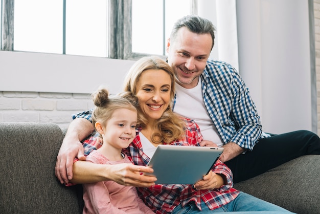 Gelukkige familie die digitale tablet op bank in woonkamer gebruiken