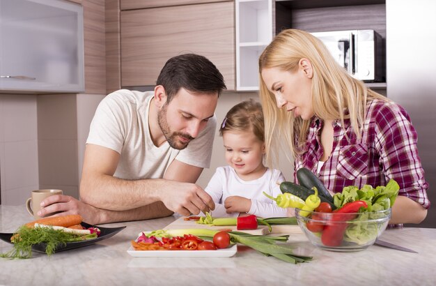 Gelukkige familie die een salade met verse groenten op het aanrecht maakt