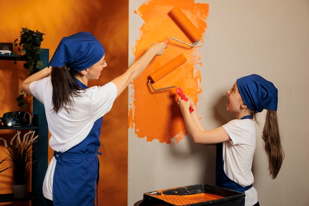 Gelukkige familie die thuis oranje muren schildert, met rolborstel en verfkleur om het appartement te versieren. Vrouw met jong kind die plezier heeft in het samen renoveren van huis, interieur van het huis.