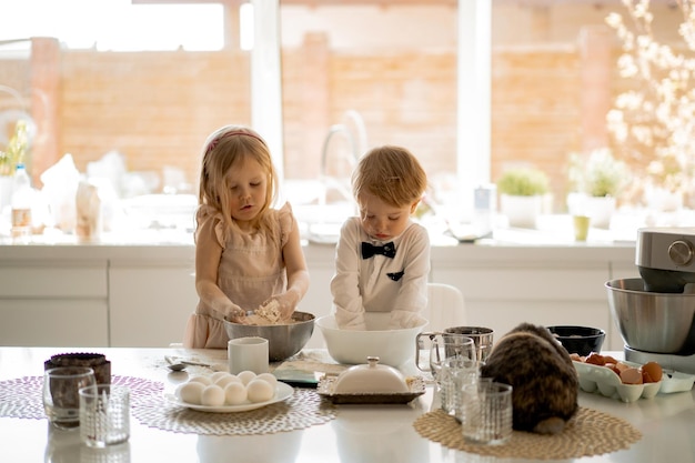 Gelukkige familie die zich voorbereidt op de paasvakantie. moeder met kinderen in de keuken bakt taarten en beschildert eieren. gedomesticeerde konijnen