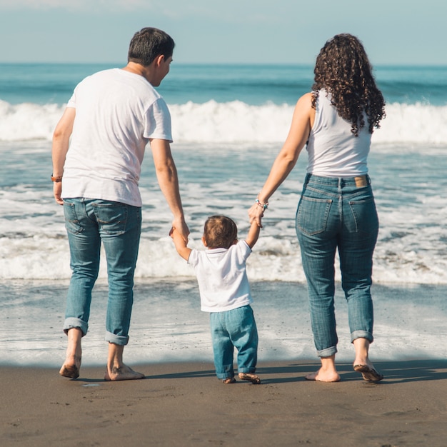 Gelukkige familie met baby die op strand loopt en op overzees kijkt