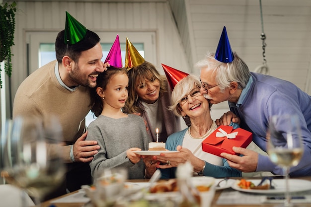 Gelukkige familie van meerdere generaties die de verjaardag van oma viert en haar verrast met verjaardagstaart en cadeaus