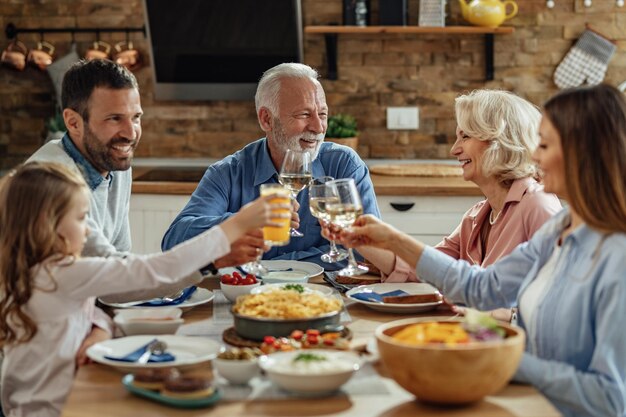 Gelukkige familie van meerdere generaties roosteren terwijl u geniet van de lunch in de eetkamer.