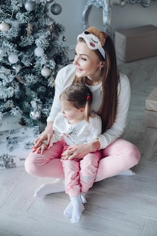 Gelukkige feestelijke moeder en dochter knuffelen samen zitten bij het versieren van mooie kerstboom