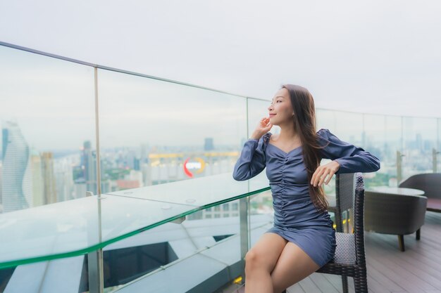 Gelukkige glimlach van de portret de mooie jonge Aziatische vrouw op dak hoogste restaurant rond stadsmening