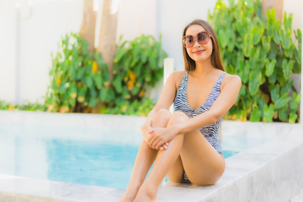Gelukkige glimlach van de portret ontspant de mooie jonge Aziatische vrouw rond openluchtzwembad in hoteltoevlucht