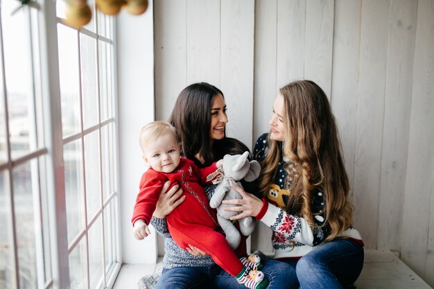 Gelukkige glimlachende familie bij studio op achtergrond van de Kerstboom met gift