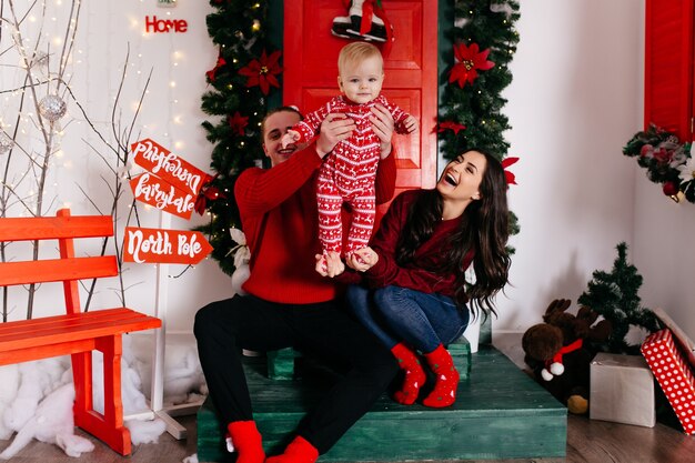 Gelukkige glimlachende familie bij studio op achtergrond van de Kerstboom met gift