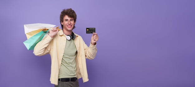 Gelukkige glimlachende knappe man die boodschappentassen draagt en creditcard toont