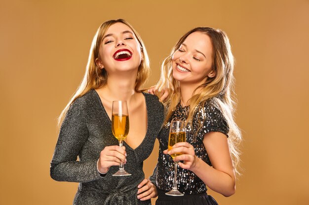 Gelukkige glimlachende vrouwen in stijlvolle glamoureuze jurken met champagneglazen
