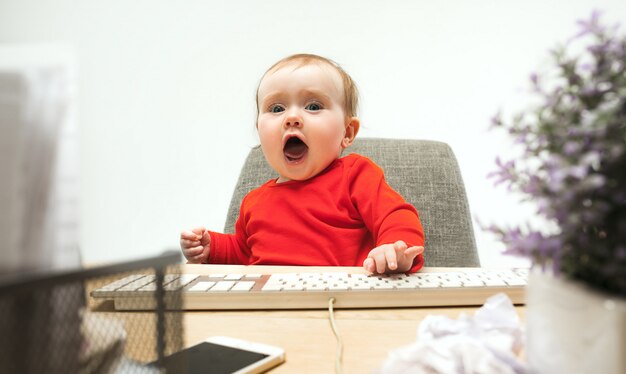 Gelukkige het meisjeszitting van de kindbaby met toetsenbord van moderne computer of laptop die op een witte studio wordt geïsoleerd