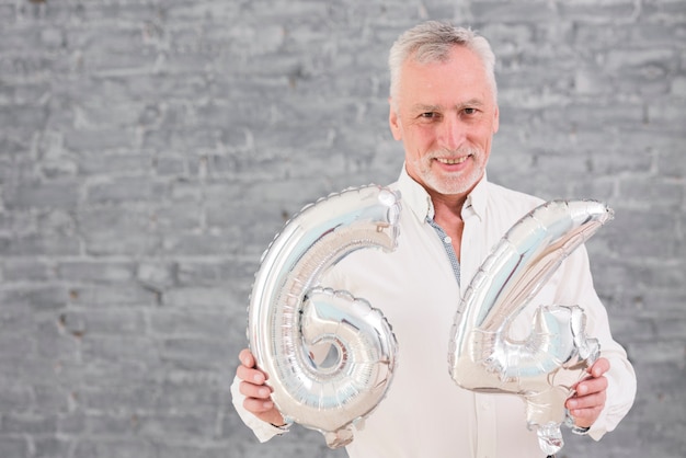 Gelukkige hogere mens die zilveren folieballon op zijn 64 verjaardag houdt