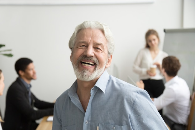 Gelukkige hogere zakenman lachen die camera in bureau, portret bekijkt