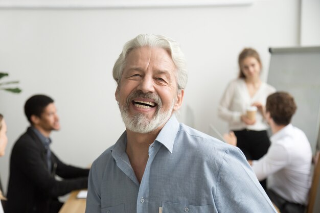 Gelukkige hogere zakenman lachen die camera in bureau, portret bekijkt