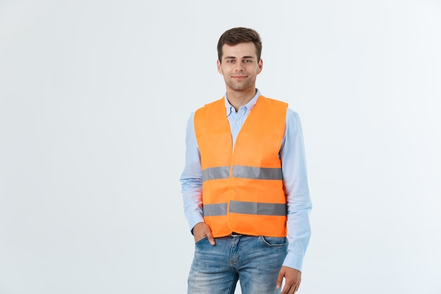 Gelukkige ingenieur glimlacht en staat vol vertrouwen, man met een caro-shirt en spijkerbroek met oranje vest, geïsoleerd op een witte achtergrond.