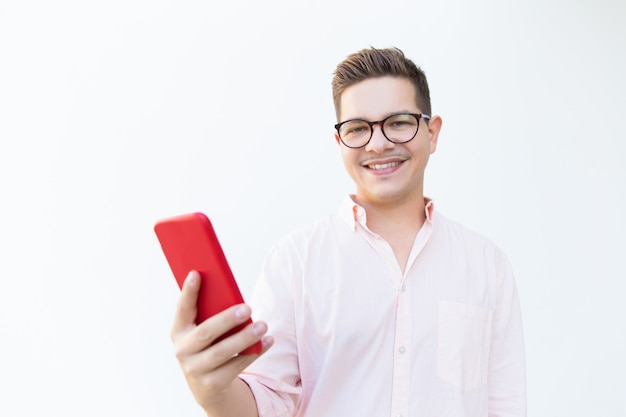 Gelukkige inhoudskerel die in oogglazen rode mobiele telefoon houden