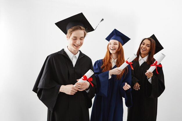Gelukkige internationale afgestudeerden die verheugd het houden van diploma's glimlachen.