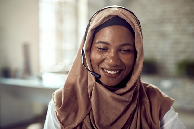 Gelukkige islamitische zakenvrouw die een headset draagt terwijl ze op kantoor werkt